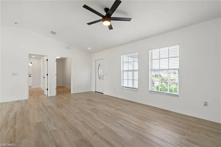 Unfurnished living room featuring ceiling fan, light hardwood / wood-style floors, and vaulted ceiling
