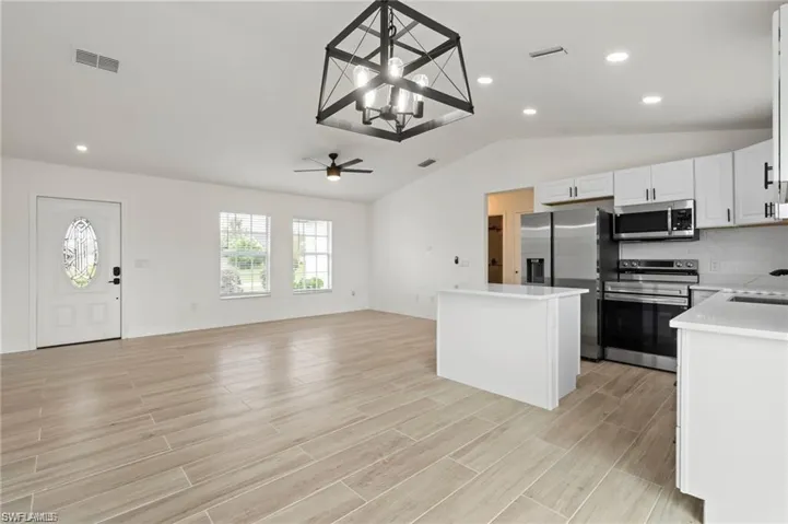 Kitchen with ceiling fan with notable chandelier, white cabinetry, light hardwood / wood-style flooring, a kitchen island, and appliances with stainless steel finishes