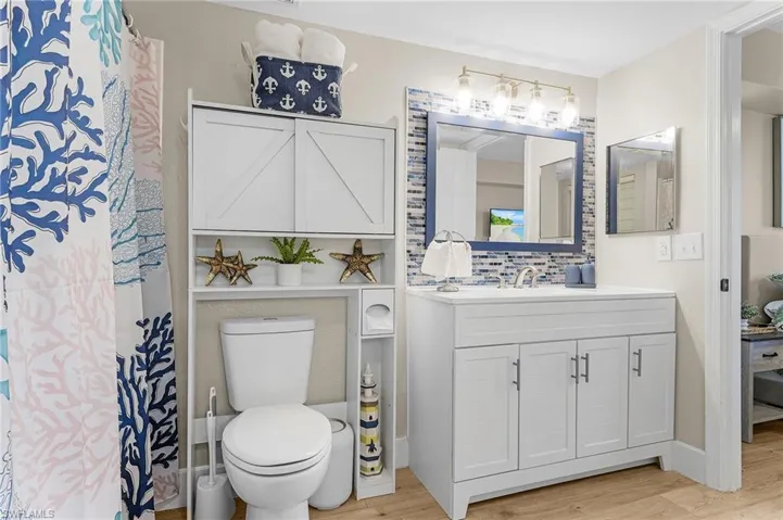 Bathroom with toilet, decorative backsplash, wood finished floors, and vanity