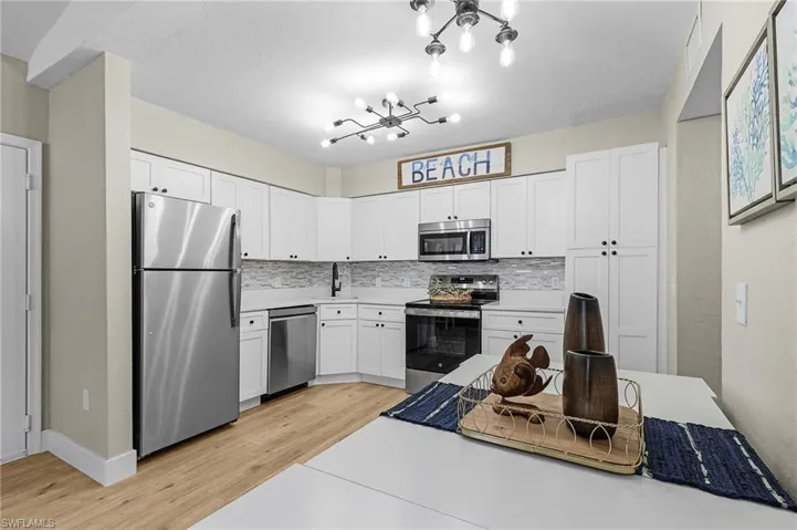 Kitchen featuring appliances with stainless steel finishes, a chandelier, white cabinetry, and light wood finished floors
