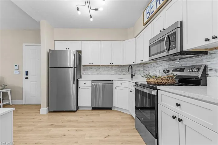 Kitchen with stainless steel appliances, light wood-style flooring, decorative backsplash, white cabinetry, and a sink