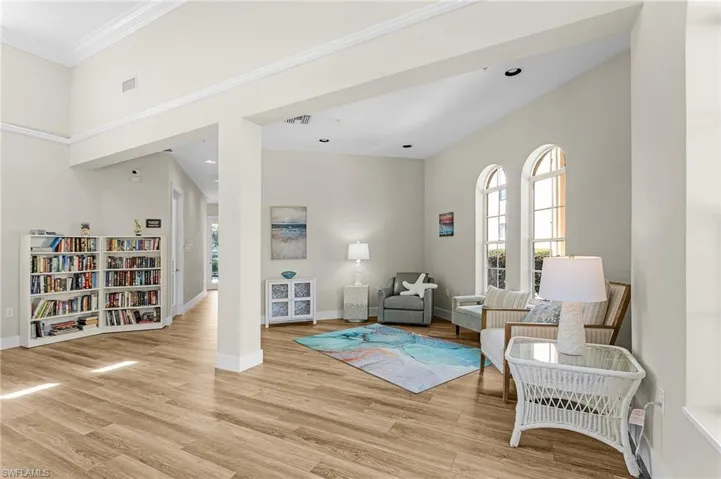 Living area with light wood finished floors, visible vents, baseboards, and crown molding