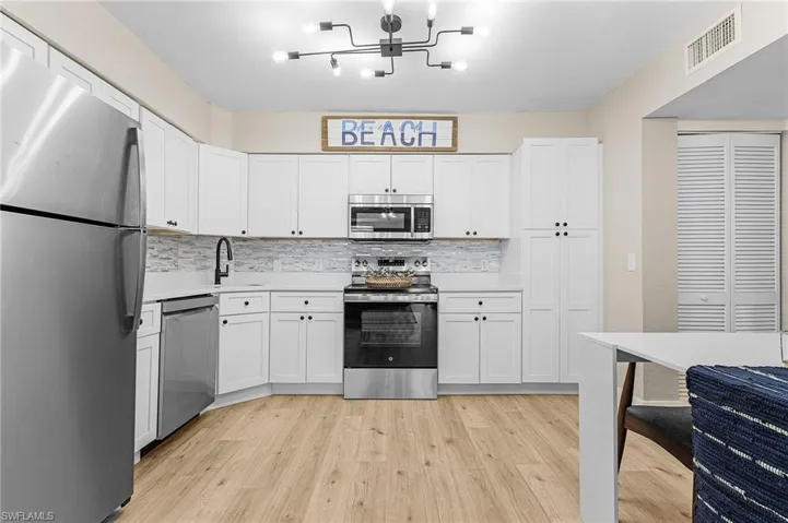 Kitchen with light countertops, visible vents, light wood-style flooring, appliances with stainless steel finishes, and a sink