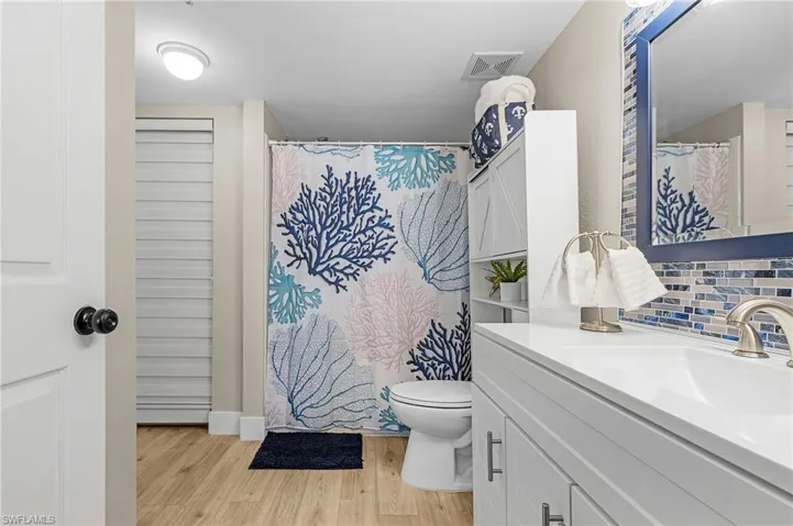 Bathroom with tasteful backsplash, visible vents, toilet, vanity, and wood finished floors