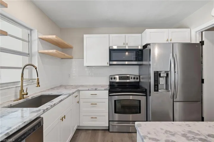 Kitchen with light hardwood / wood-style floors, light stone countertops, appliances with stainless steel finishes, decorative backsplash, and sink