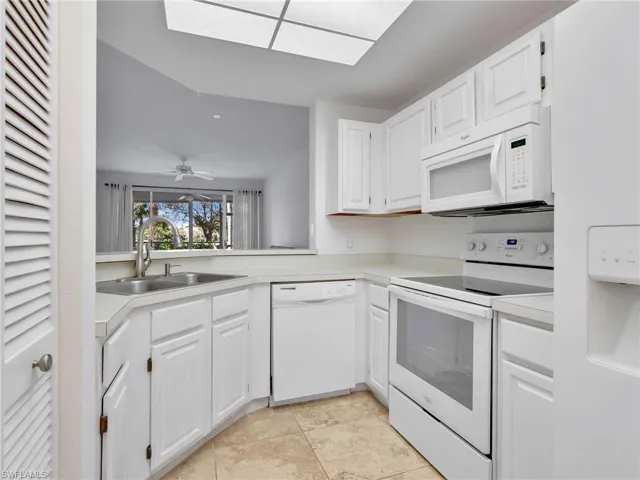 Kitchen with white appliances, white cabinets, light countertops, a skylight, and ceiling fan