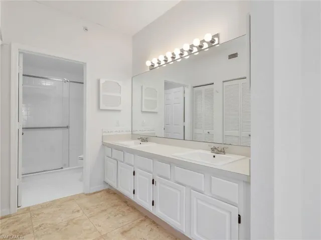 Full bathroom featuring double vanity, light tile patterned flooring, a stall shower, and a closet