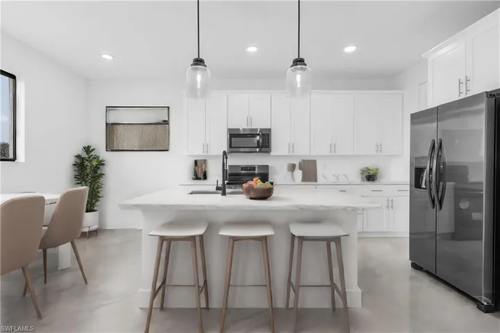 Kitchen with an island with sink, hanging light fixtures, stainless steel appliances, and white cabinetry
