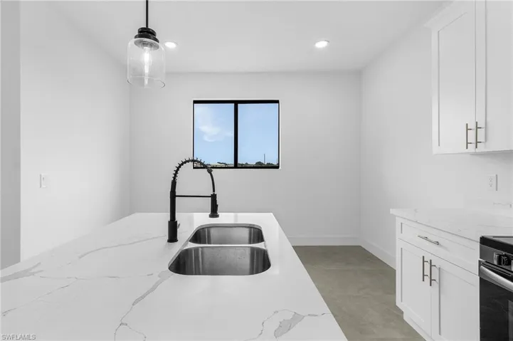 Kitchen featuring light tile patterned floors, light stone countertops, white cabinetry, sink, and pendant lighting