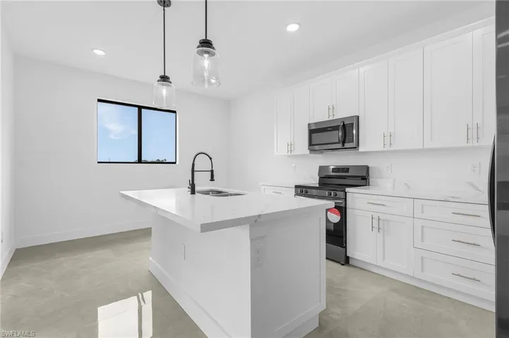 Kitchen featuring appliances with stainless steel finishes, light stone counters, white cabinetry, sink, and a center island with sink
