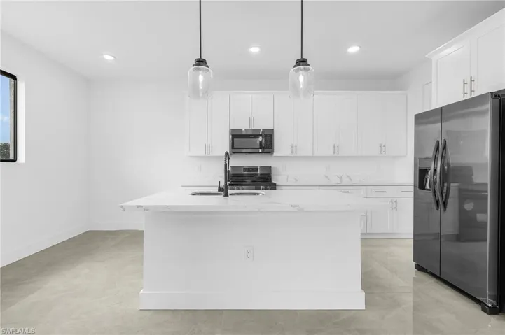 Kitchen featuring white cabinetry, decorative light fixtures, light stone counters, appliances with stainless steel finishes, and a center island with sink