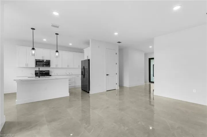 Kitchen featuring decorative light fixtures, a center island with sink, black appliances, light tile patterned floors, and white cabinetry