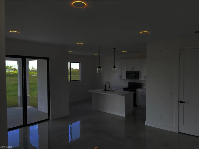 Kitchen with black appliances, sink, an island with sink, hanging light fixtures, and white cabinets