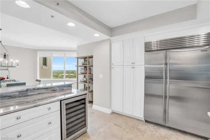 Kitchen featuring white cabinets, built in refrigerator, light tile patterned floors, light stone countertops, and beverage cooler