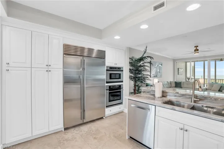 Kitchen featuring appliances with stainless steel finishes, sink, light stone counters, white cabinetry, and ceiling fan