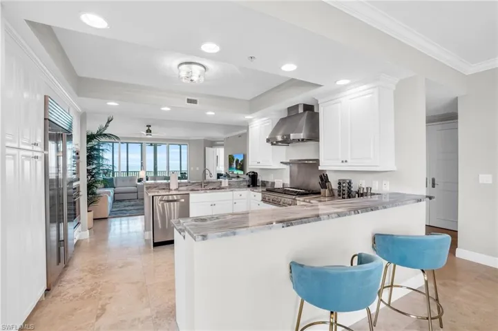 Kitchen with white cabinetry, kitchen peninsula, wall chimney range hood, and stainless steel appliances