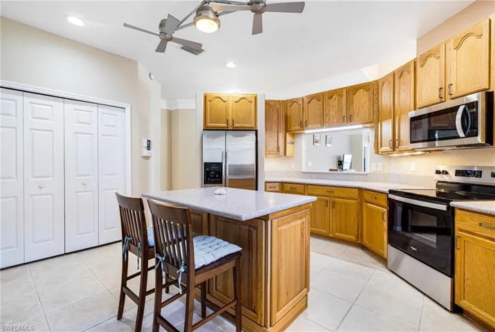 Kitchen featuring a breakfast bar area, ceiling fan, light tile patterned floors, a kitchen island, and stainless steel appliances