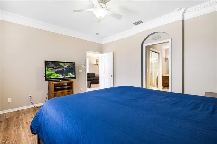 Bedroom with ensuite bath, hardwood / wood-style floors, crown molding, and ceiling fan