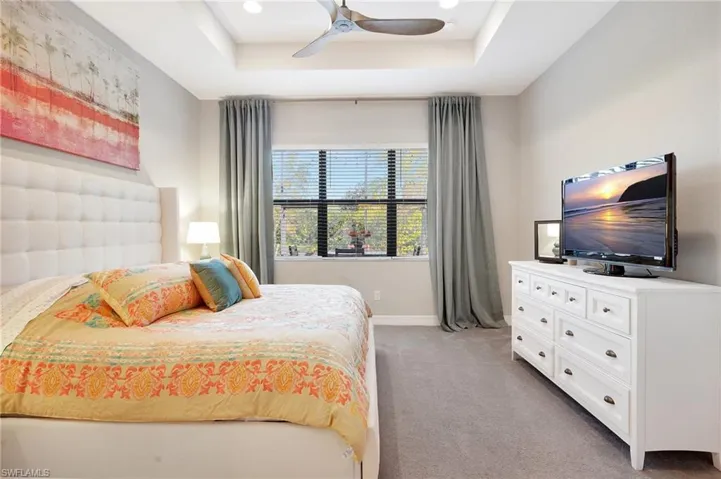 Bedroom with baseboards, a raised ceiling, a ceiling fan, and light colored carpet