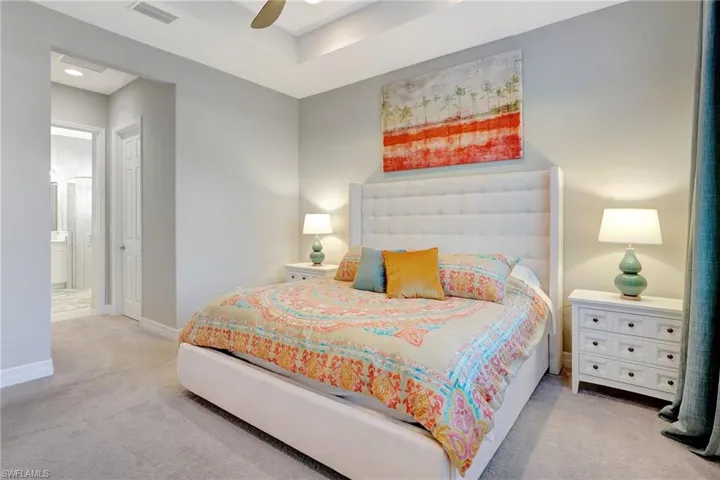 Carpeted bedroom featuring a ceiling fan, ensuite bath, visible vents, and baseboards