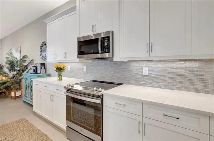 Kitchen featuring stainless steel appliances, backsplash, light stone countertops, and white cabinets