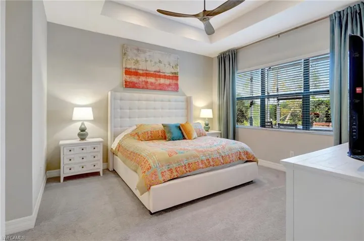 Bedroom featuring a raised ceiling, light carpet, ceiling fan, and baseboards