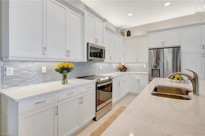 Kitchen featuring light stone countertops, appliances with stainless steel finishes, backsplash, and a sink