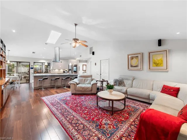 Living area featuring a skylight, a ceiling fan, dark wood-type flooring, recessed lighting, and vaulted ceiling