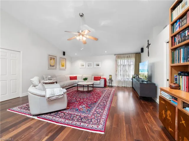 Living room featuring a ceiling fan, dark wood-type flooring, and lofted ceiling