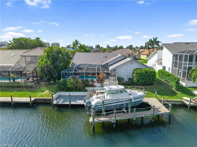 Rear view of house with glass enclosure, a water view, an outdoor pool, and boat lift