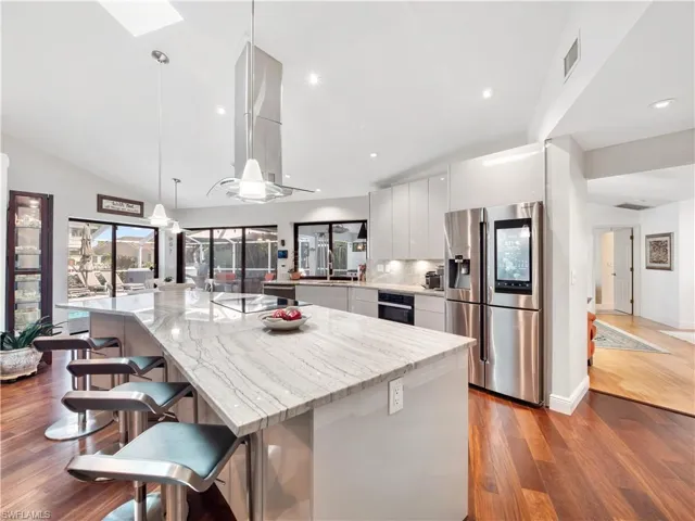 Kitchen with stainless steel fridge, a breakfast bar, dark wood-type flooring, white cabinetry, and a large island