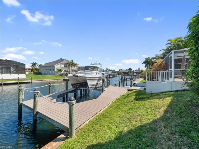 Dock featuring a water view, boat lift, glass enclosure, and a lawn