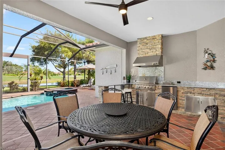Screened patio featuring an outdoor kitchen with stainless steel appliances, stone accents, and built-in cabinetry