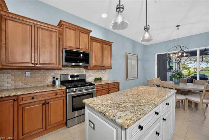 Gourmet kitchen featuring a central island with granite countertop, stainless steel gas range, wood cabinetry, stone tile backsplash, and ceramic tile flooring