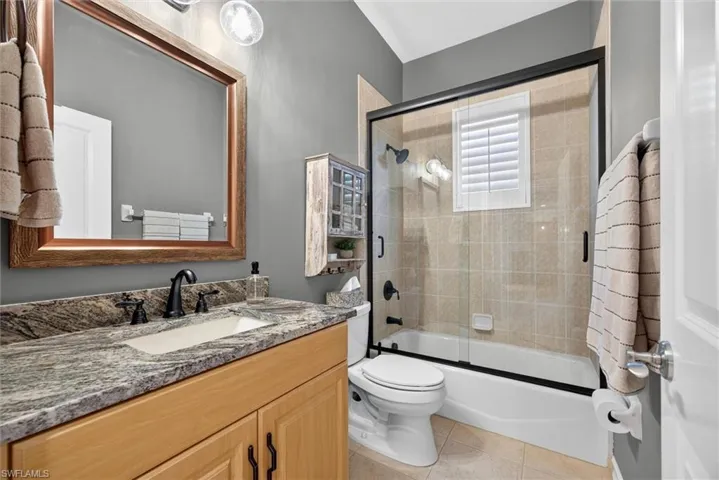Bathroom featuring a wood-finish vanity with stone countertop, undermount sink, and matte black faucet