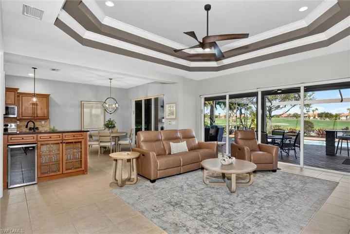 Open-concept living area with a coffered ceiling, tile flooring, and a built-in wet bar featuring wood cabinetry and a beverage cooler