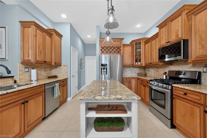 Expansive kitchen featuring a central island with a granite countertop, wood cabinetry, stainless steel appliances, tile flooring, and recessed lighting
