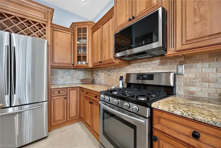 Kitchen featuring stainless steel appliances, granite countertops, tile backsplash, wood cabinetry, and a built-in wine rack