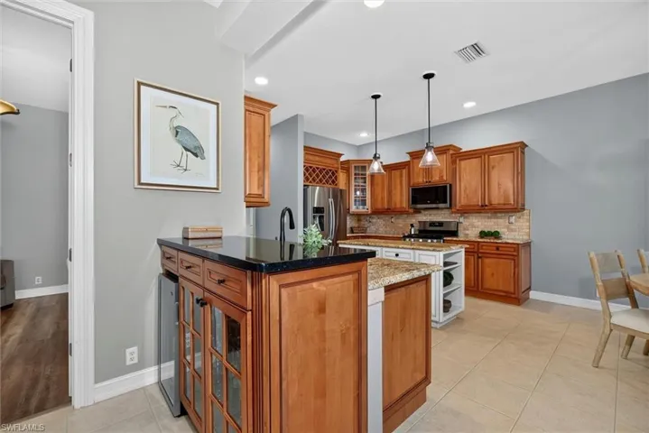 Kitchen featuring warm wood cabinetry, a central island with granite countertop and pendant lighting, stainless steel appliances, and tile flooring