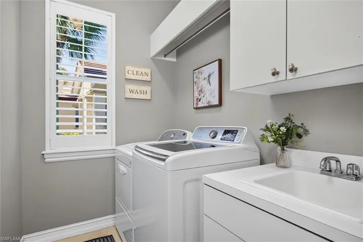 Dedicated laundry room featuring a utility sink with dual-handle faucet, white cabinetry, and a window with plantation shutters