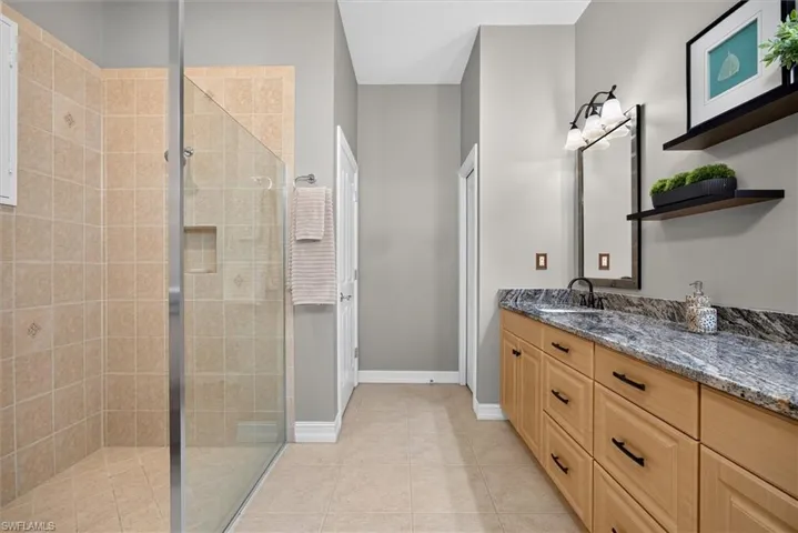Neutral-toned tile flooring complemented by a glass-enclosed shower with tiled walls and a built-in niche