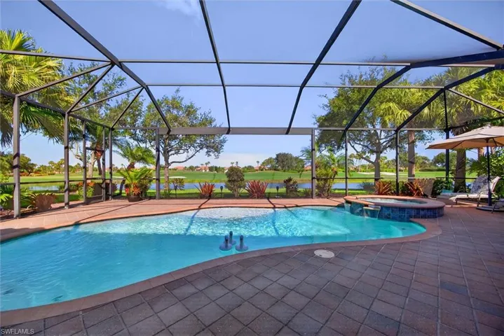 Screened pool enclosure featuring a curvilinear pool, integrated spa with waterfall, and paver patio