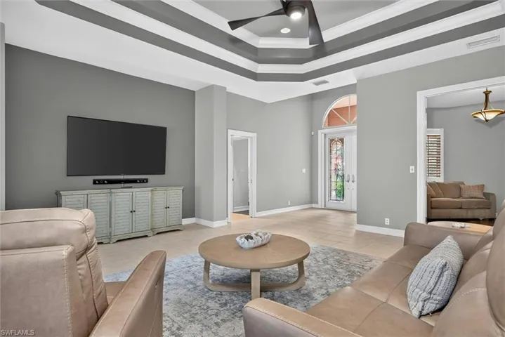 Living area featuring a tiered tray ceiling with recessed lighting, a ceiling fan, and tile flooring