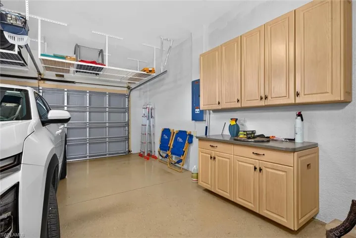 Garage featuring a neutral-toned epoxy floor, light wood-finish cabinetry, and overhead storage racks