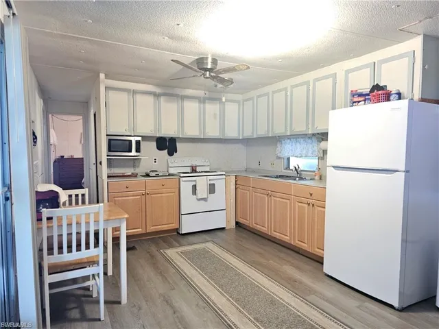 Kitchen with white appliances, a textured ceiling, light countertops, light wood-style flooring, and ceiling fan