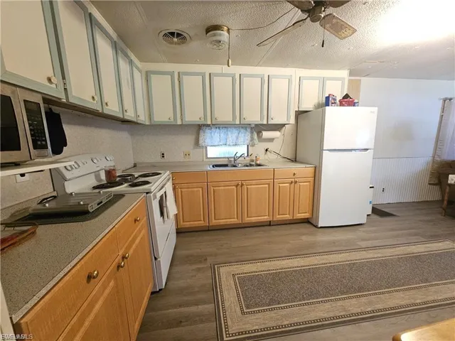 Kitchen featuring white appliances, ceiling fan, dark wood-style floors, light countertops, and a textured ceiling
