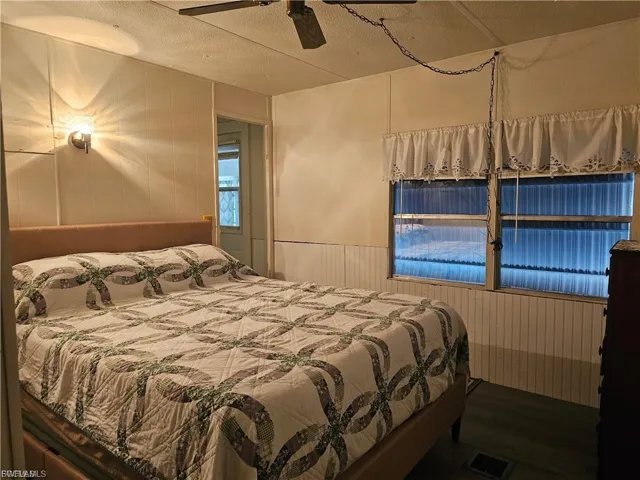 Bedroom featuring a decorative wall, ceiling fan, wooden walls, wood finished floors, and a textured ceiling