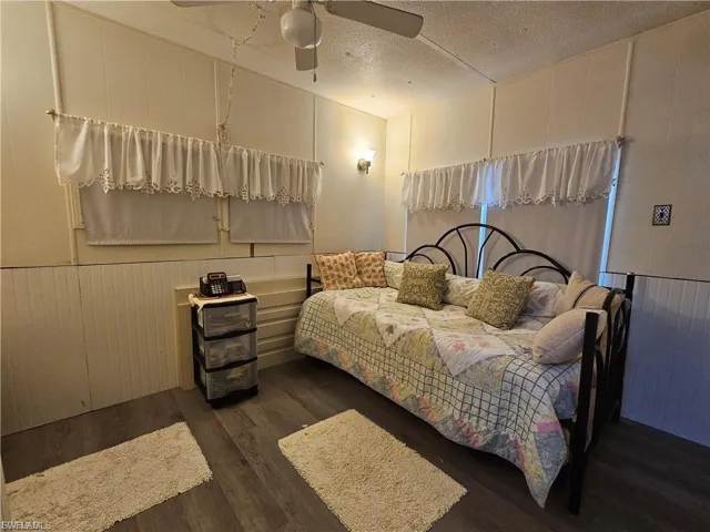 Bedroom with a textured ceiling, a decorative wall, dark wood-style flooring, a ceiling fan, and wooden walls