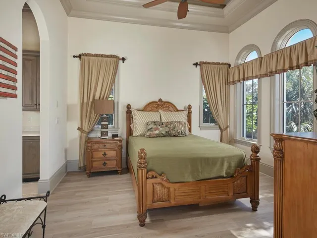 Bedroom with light wood-type flooring, ornamental molding, a ceiling fan, and arched walkways