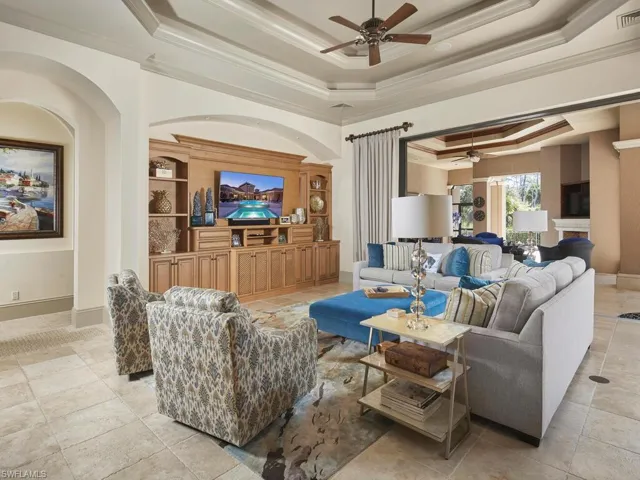 Living room featuring a ceiling fan, a tray ceiling, ornamental molding, a fireplace, and light tile patterned flooring